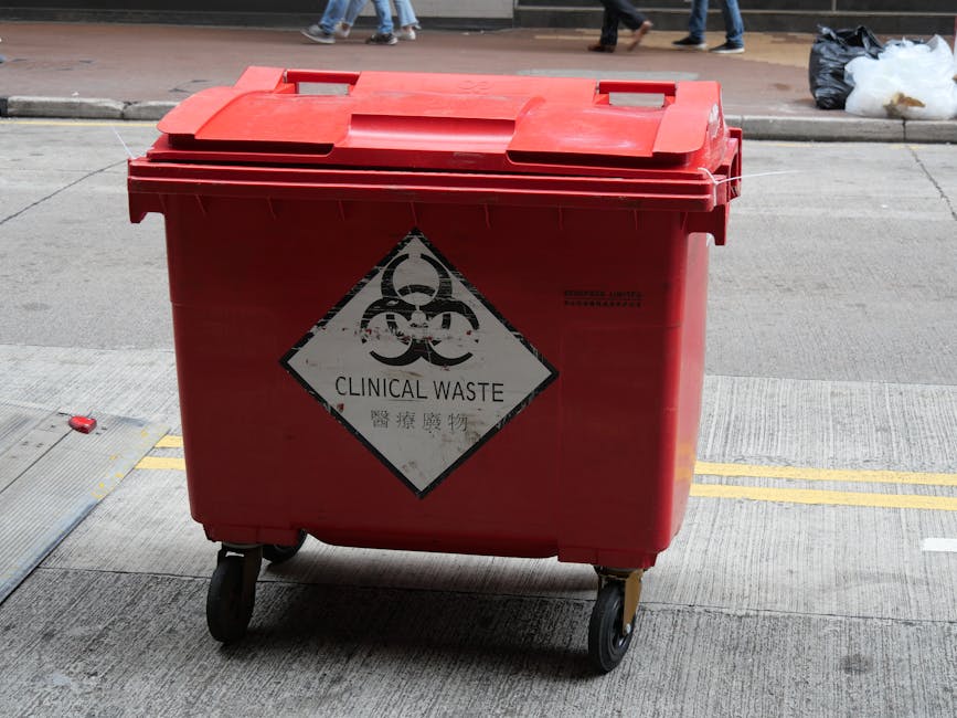 A street cleaning worker from Cleaners Merton dressed in an orange high-visibility suit and safety helmet is sweeping debris from the curb using a long-handled broom. The worker is positioned on the e